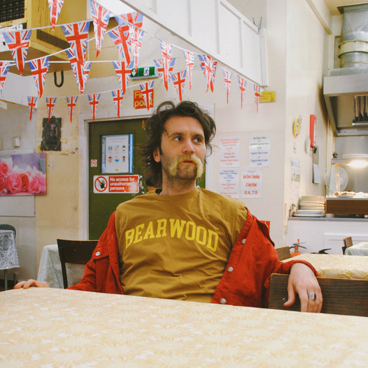 Tat Vision wear Brumbox's Bearwood athletic varsity style logo printed in yellow on the chest of a mustard t-shirt (front)